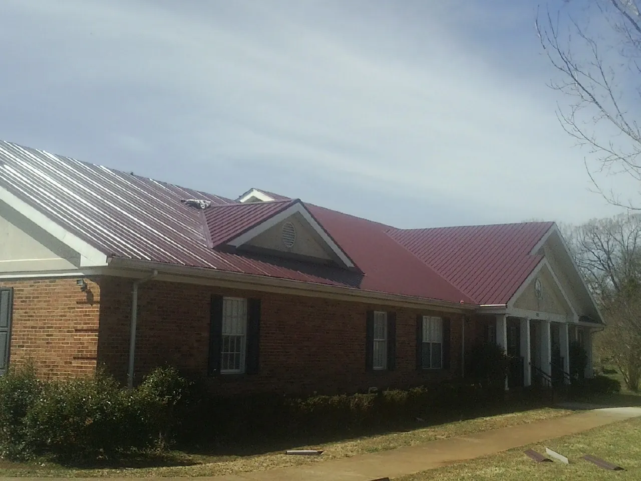 Red metal roof with gabled entries on a long brick building, from a Hail Damage Roof Repair job in Bowman