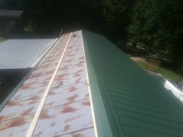Old rusted panels beside newly installed green metal roofing — Wind Damage Roof Repair by Roofing Brothers in Bowman